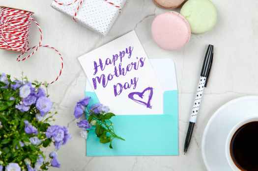 happy mothers day card beside pen macaroons flowers and box near coffee cup with saucer